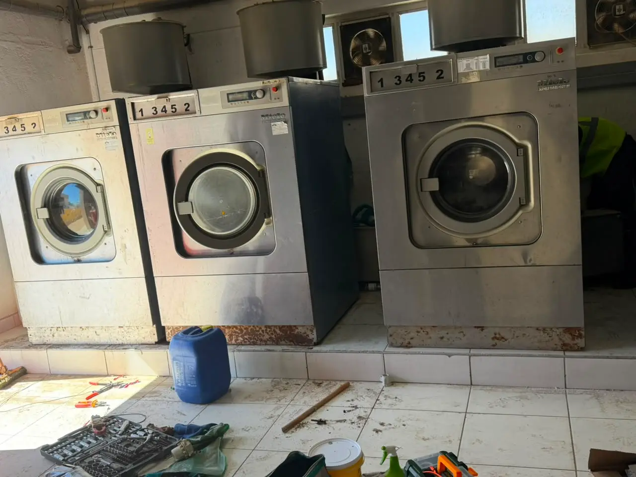 Three industrial washing machines with service tools laid out on the floor