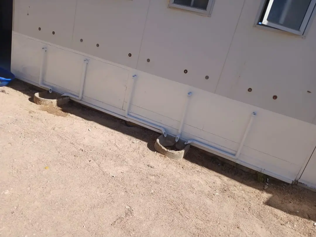 Exterior wall of the shower block with painted drainage pipework and concrete drain bowls