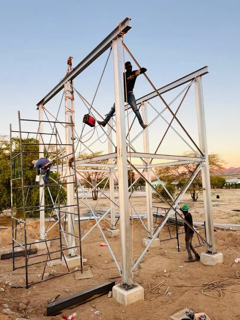 Workers fabricating a galvanised steel tower frame at sunset