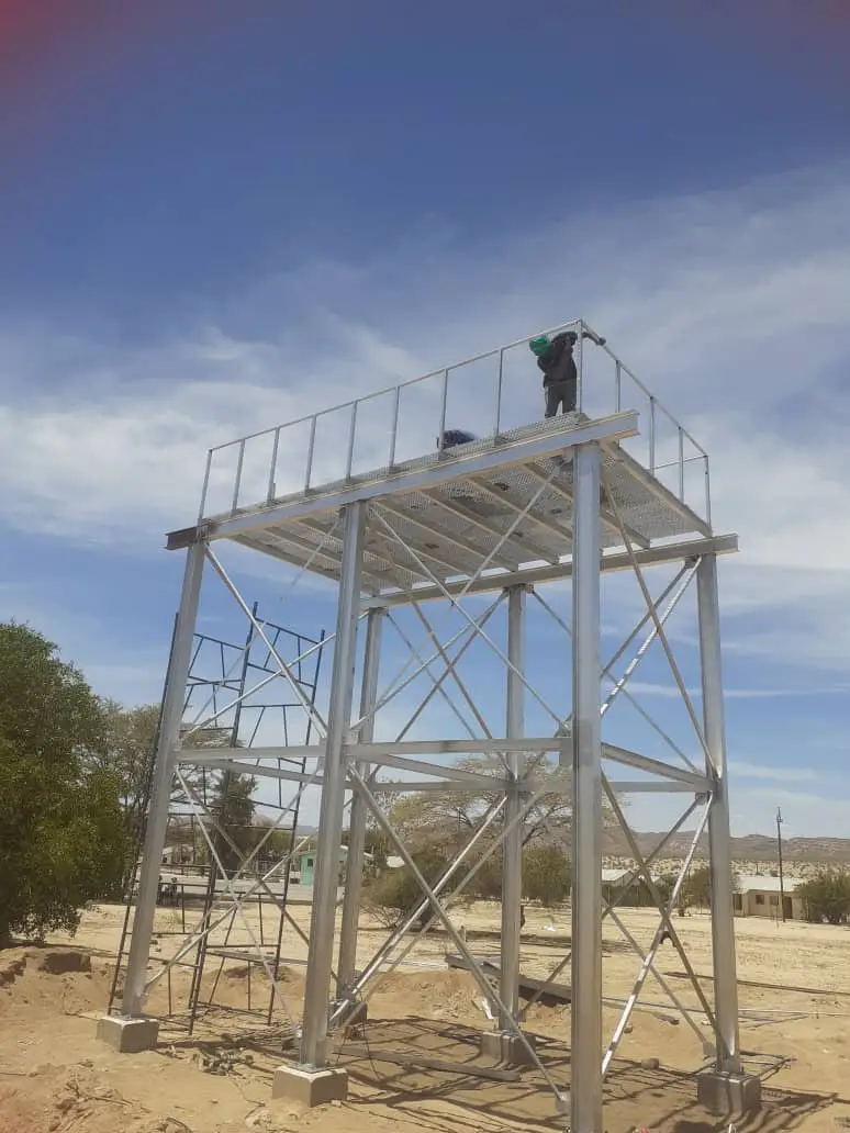 Galvanised steel tower with a worker on the top platform under a blue sky