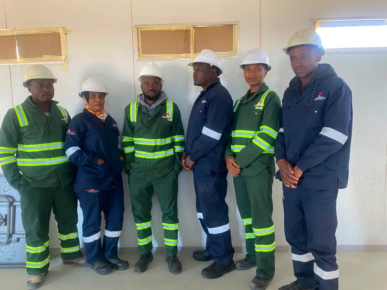 Six team members in green and navy Mundesha workwear and hard hats, third pose