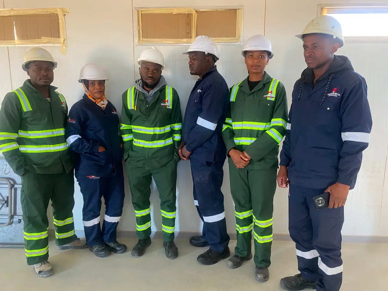 Six team members in green and navy Mundesha workwear and hard hats, second pose