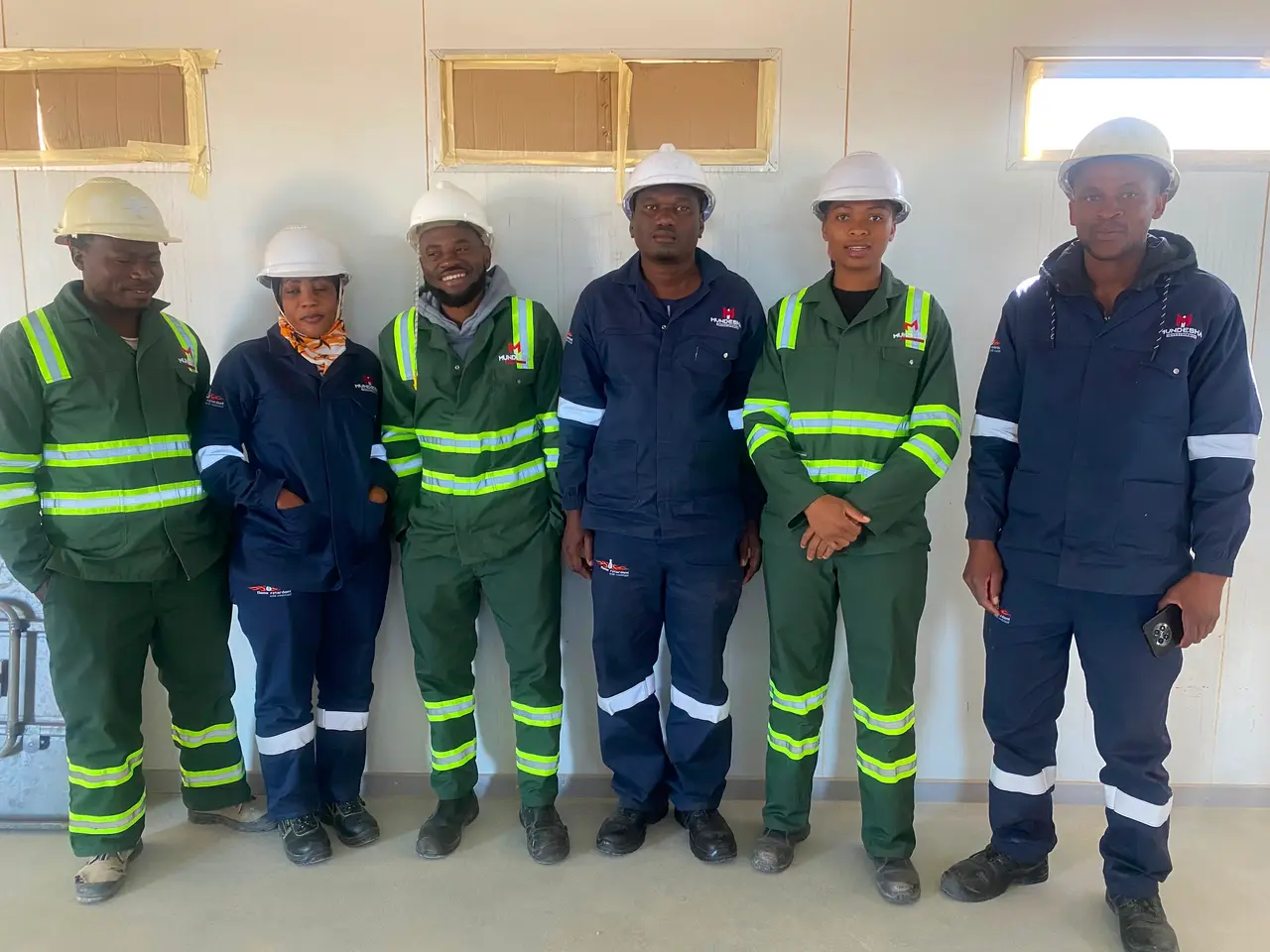 Six team members in green and navy Mundesha workwear and hard hats