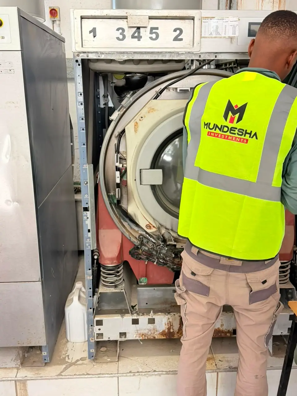 Technician in a Mundesha hi-vis vest working on an opened industrial washing machine