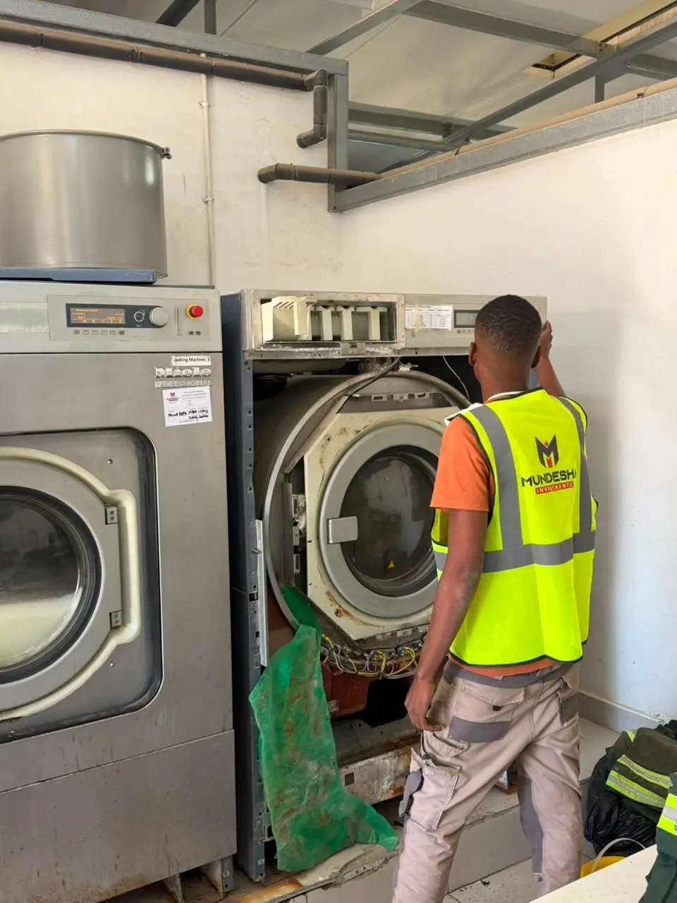 Technician in a Mundesha hi-vis vest servicing an industrial washing machine