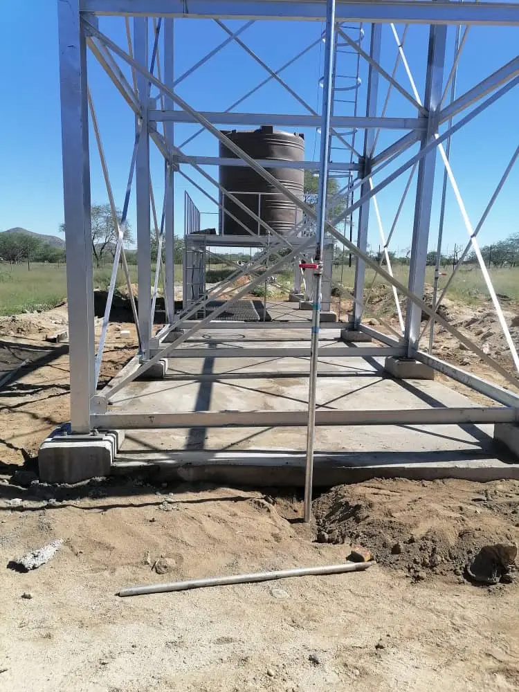 Concrete base slab and galvanised steel frame of a water tank stand with a tank in the background