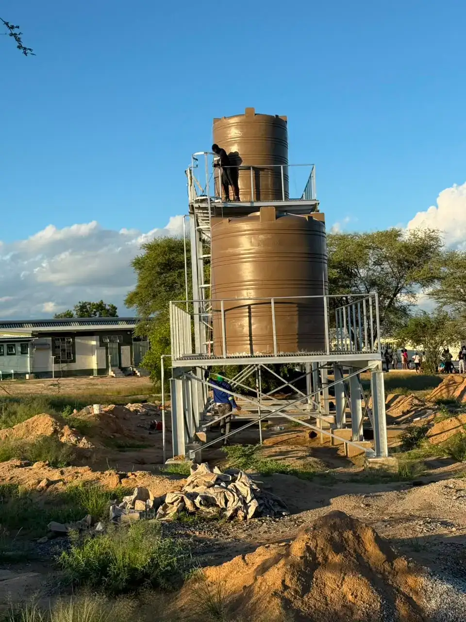 Two brown water tanks on a galvanised steel stand with a worker on the upper platform