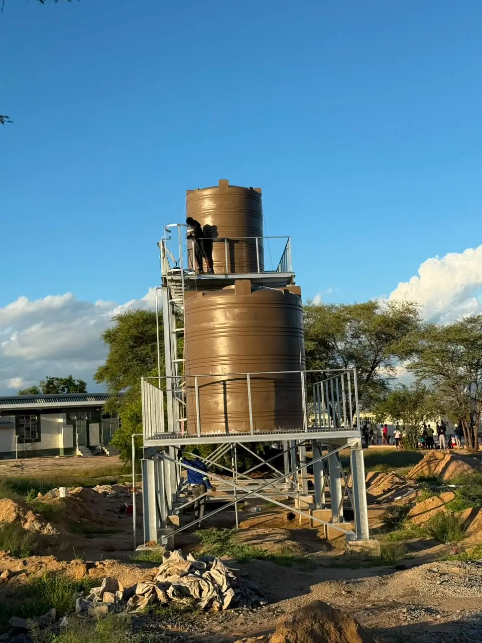 Two brown water tanks on a galvanised steel stand, wider view with worker on the platform