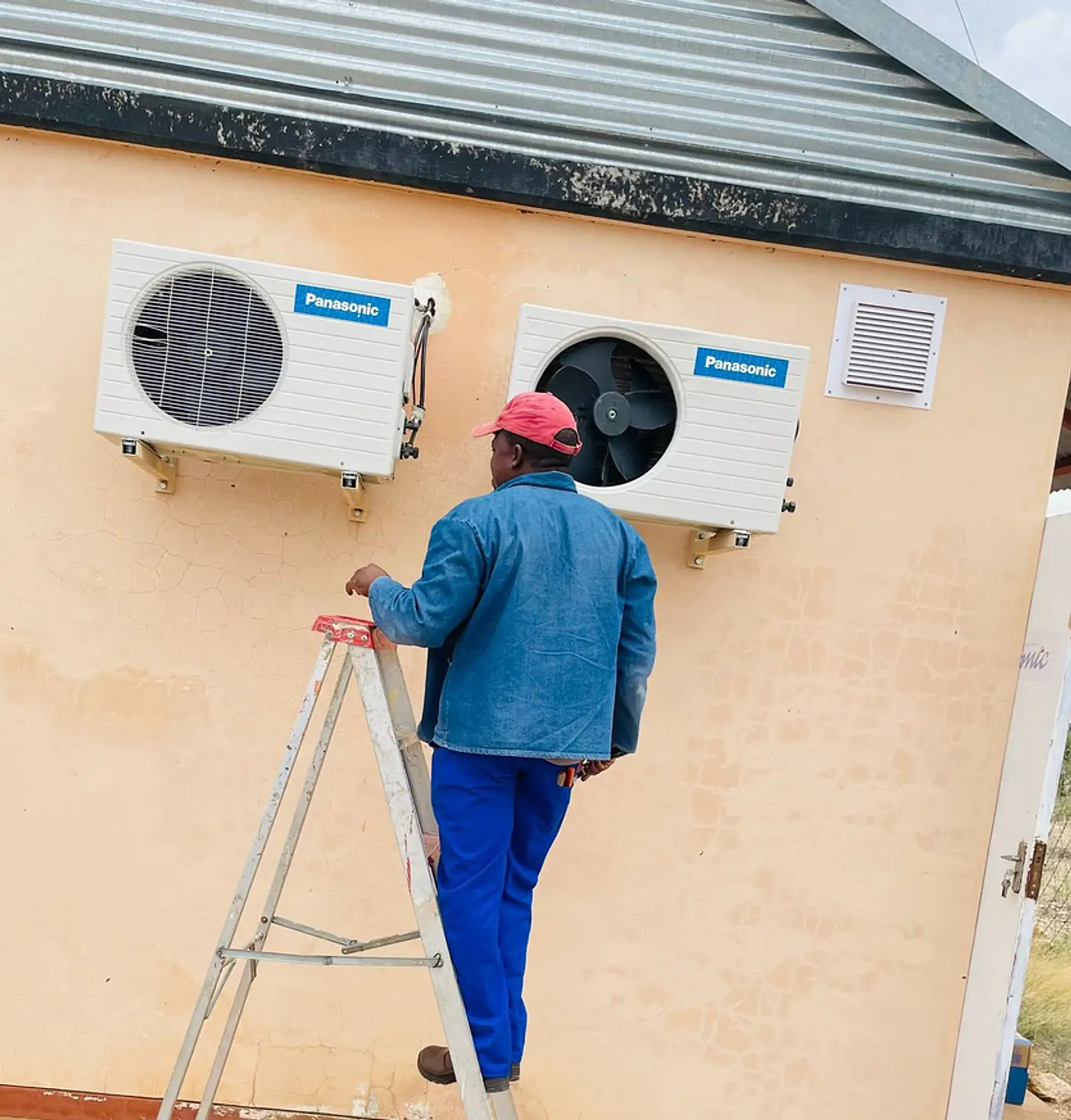 Technician on a ladder servicing wall mounted air conditioning units